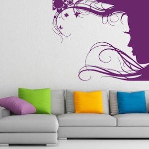 May include: A purple silhouette of a woman with flowing hair and floral accents on a white wall above a gray couch with colorful throw pillows.