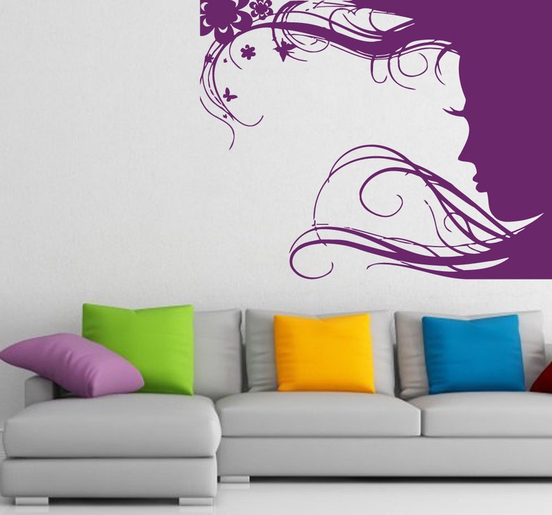 May include: A purple silhouette of a woman with flowing hair and floral accents on a white wall above a gray couch with colorful throw pillows.