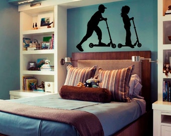 May include: A bedroom with a blue wall and a bed with brown bedding. There is a white bookshelf with books and a wall decal of two children riding scooters.