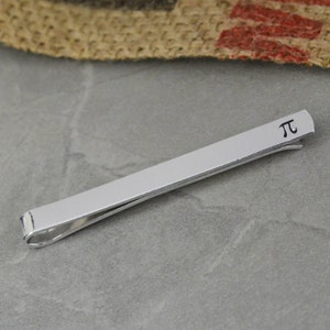 May include: A silver tie bar with a simple design featuring the mathematical symbol pi.