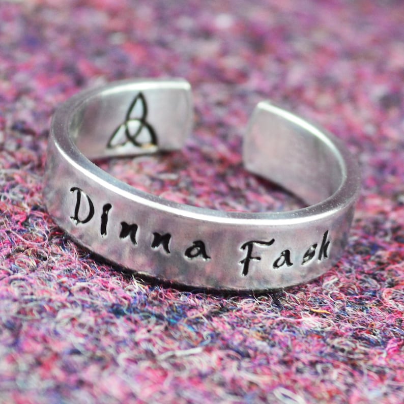 May include: A silver ring inscribed with the words "Dinna Fask" and a Celtic knot design on the inside.