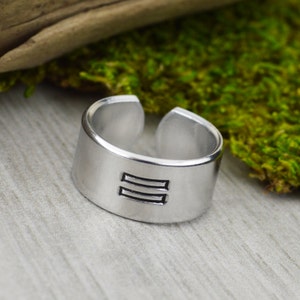 May include: A silver ring with a simple design of two parallel lines engraved on the band.