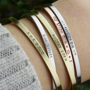 May include: Five gold, silver, and rose gold bangle bracelets with engraved messages. The bracelets read "Ride or Die", "My Tribe", "Audrey Eden", "Soul Sisters", and "x♡x♡x♡".