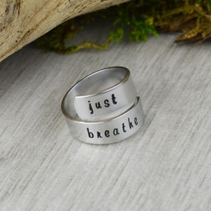 May include: A silver-toned ring with the words "just breathe" engraved on it. The ring is designed to be worn on the finger and is a reminder to take a moment to breathe.