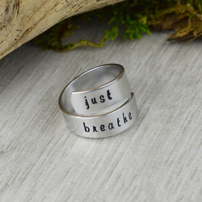May include: A silver-toned ring with the words "just breathe" engraved on it. The ring is designed to be worn on the finger and is a reminder to take a moment to breathe.