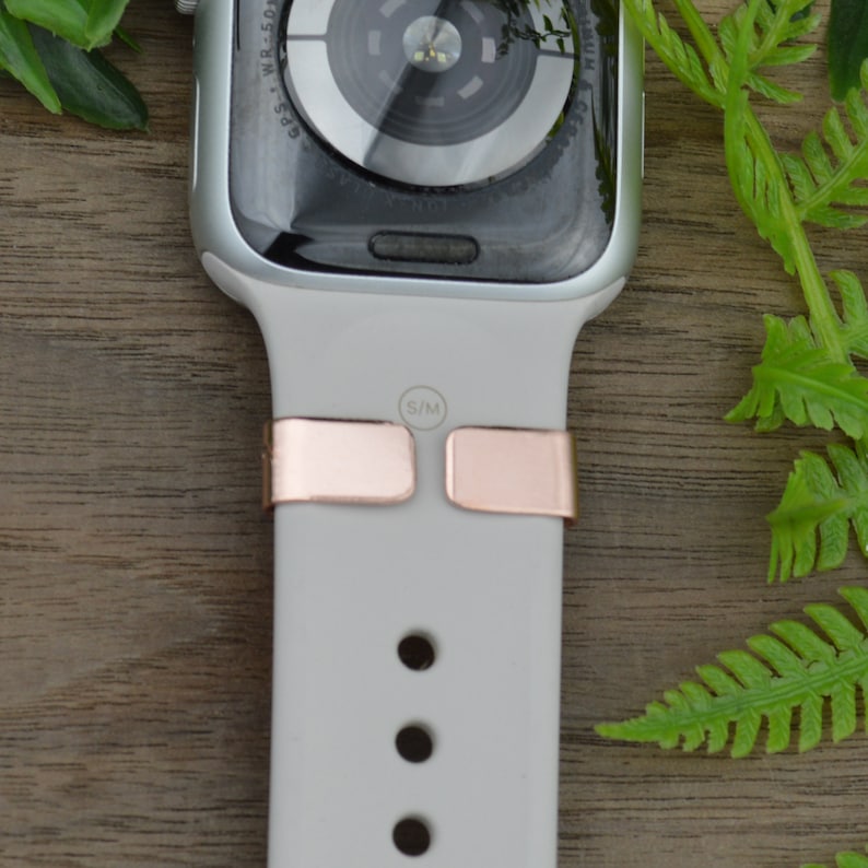 K&ouml;nnte beinhalten: Ein wei&szlig;es Apple Watch Armband mit ros&eacute;goldenen Metallschlie&szlig;en. Das Armband hat eine Gr&ouml;&szlig;enangabe mit "S/M".