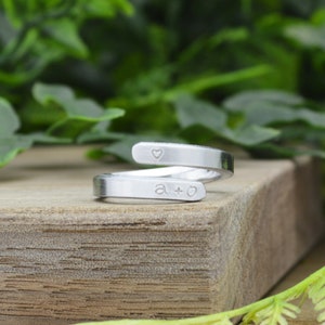 May include: A silver ring with a heart and the letters "a + o" engraved on it. The ring is wrapped around a wooden surface.