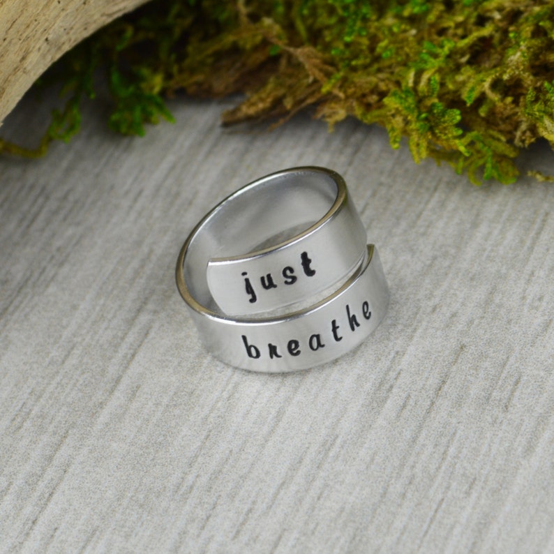 May include: A silver ring with the words "just breathe" engraved on it. The ring is designed to be worn on the finger and is a reminder to take a deep breath and relax.