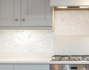 May include: A white kitchen with gray cabinets and a stainless steel oven and stovetop. The countertop is white and the backsplash is white with gray veining.