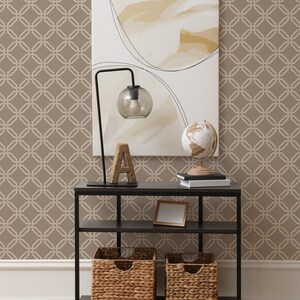 May include: A black metal console table with two shelves. The top shelf has a globe, a lamp with a glass shade, and a wooden letter A. The bottom shelf has two woven baskets and a framed picture. The table is in front of a wall with a brown geometric wallpaper pattern.