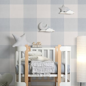 May include: A white crib with a wooden base and a white and gray gingham patterned wall. The crib has a white mattress and a white blanket with a fringe. There are two white shelves with a crescent moon and a star on them.