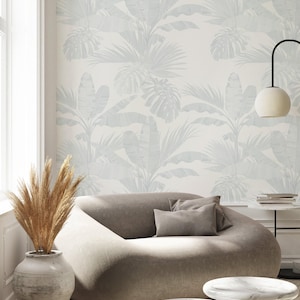 Könnte beinhalten: Modernes Wohnzimmer mit hellgrauem Sofa und passenden Kissen, zwei Beistelltischen mit Marmorplatten und einer großen Vase mit getrocknetem Pampasgras. Die Tapete hat ein sich wiederholendes Muster aus hellblauen tropischen Blättern.