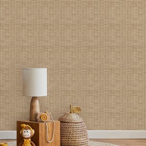 Op de afbeelding: Een bruine geweven wandbekleding met een geweven peer-vormige mand, een houten lamp met een witte lampenkap, een houten blok met een knuffel aap die een gele jurk draagt, en houten letterblokken die "NOW" spellen op een geweven tapijt.