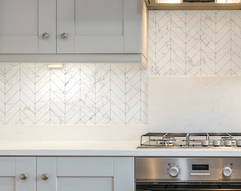 May include: A white kitchen with gray cabinets and a stainless steel oven and stovetop. The backsplash is white subway tile with a herringbone pattern.
