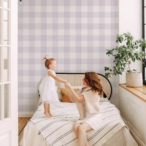 Könnte beinhalten: Eine Mutter und ihre Tochter spielen auf einem Bett mit einer weißen und lila karierten Tapete. Das Bett hat eine weiß-schwarze gestreifte Decke.