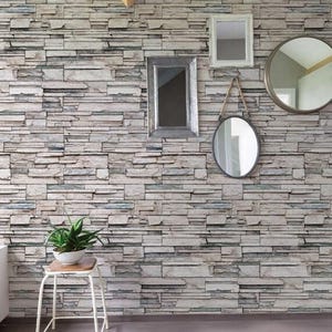 May include: A wall covered in a faux stone wallpaper with a light gray, brown, and white color scheme. There are four mirrors hanging on the wall, and a small potted plant on a white stool.