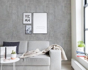 May include: A light gray sofa with a beige throw blanket, positioned against a concrete-textured wall featuring three framed prints. One print displays the text YE AH, another shows a forest, and the third contains the quote The earth has music for those who listen.