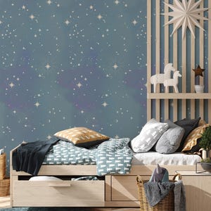 Op de afbeelding: Een lichtblauwe slaapkamer met een bed met een wit en groen gestreept dekbed en een geweven mand gevuld met dekens. De muur is bedekt met een blauwe behang met een wit sterrenpatroon.