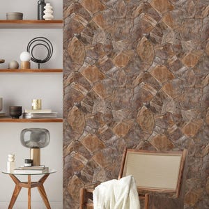 May include: A brown wicker chair with a white throw blanket sits in front of a wall covered in brown stone-patterned wallpaper. A wooden side table with a glass top sits in the foreground.