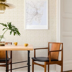 May include: A dining room with a light wood table and two chairs. The table has a black metal base and the chairs have dark wood frames and black leather seats. The wall is covered in a white wallpaper with a subtle pattern of small yellow dots. A framed map of Sydney, Australia hangs on the wall. A potted plant sits on the table.