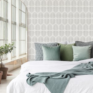 May include: A white bed with a light blue blanket and green pillows in a room with a white wall featuring a grey leaf pattern.