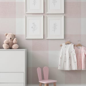 May include: A pink and white gingham wallpaper with four white picture frames with black and white line drawings of flowers. There is a white dresser with two drawers, a pink bunny chair, a teddy bear, and two white dresses hanging on hangers.