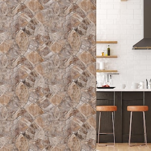 Puede incluir: Un primer plano de un papel tapiz de piedra marrón y beige con un zócalo blanco. El papel tapiz está en una cocina con paredes de azulejos blancos tipo metro, armarios marrones y dos taburetes de bar de cuero marrón.