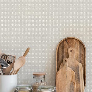 May include: A kitchen countertop with a light gray patterned wallpaper. There are three glass jars filled with grains, a white ceramic container with wooden spoons, and three wooden cutting boards.