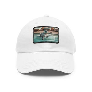 May include: White baseball cap with a rectangular patch featuring a dog wearing sunglasses, lounging on a pool float. The dog has a spotted coat and is in a pool. The cap has a curved brim and a structured crown.