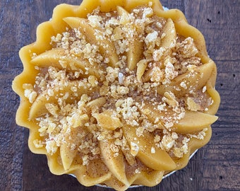 May include: A yellow candle shaped like a pie with a brown crumble topping.