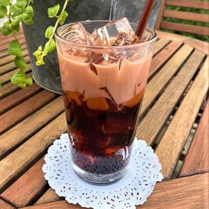 May include: A glass of iced tea with a brown straw, sitting on a white doily on a wooden table.