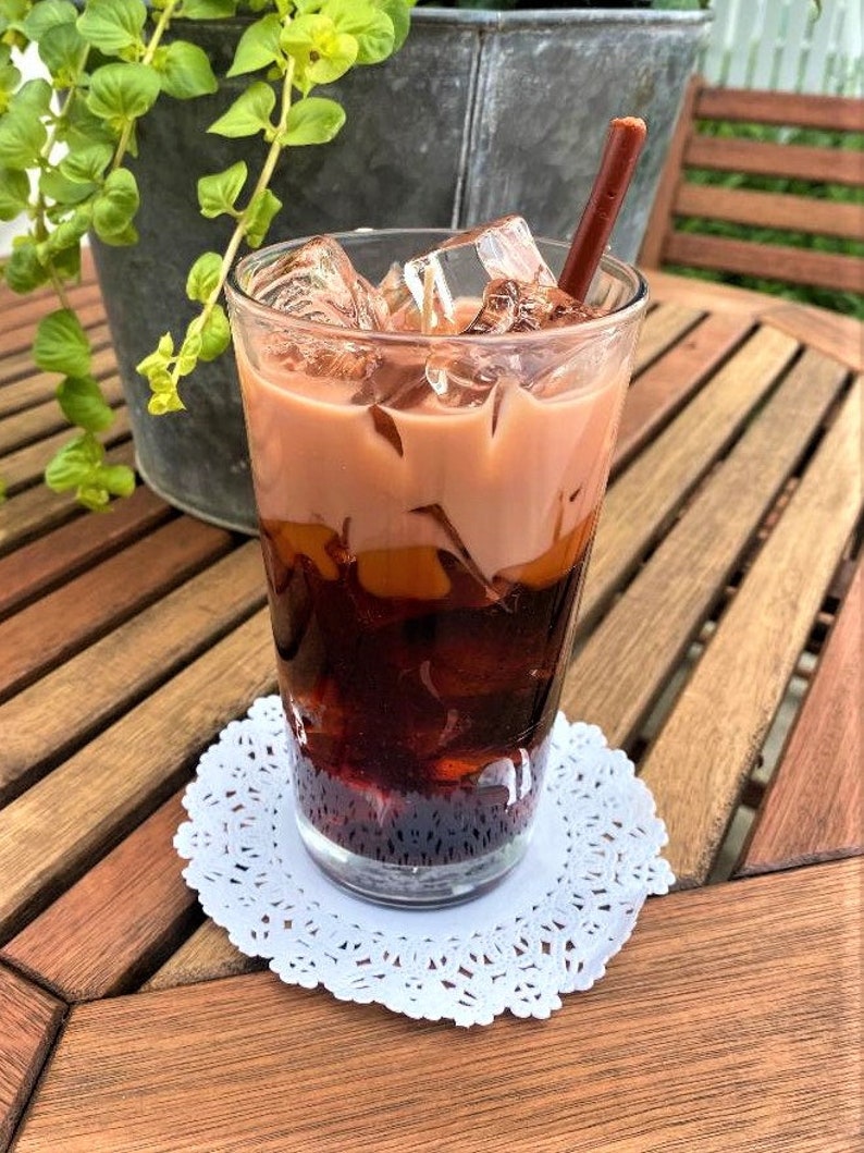 May include: A glass of iced tea with a brown straw, sitting on a white doily on a wooden table.