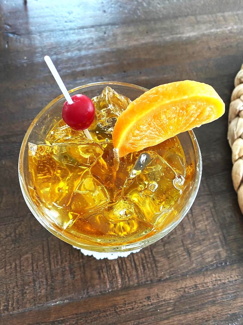 May include: A glass filled with ice and a yellow alcoholic beverage, garnished with an orange slice and a maraschino cherry.
