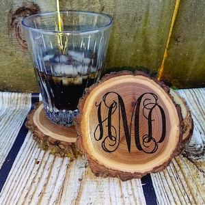 May include: Three wooden coasters with a natural bark edge. The coasters are round and have a dark brown wood grain. The center of one coaster has a monogram of the letters "HMD" in a decorative script font.