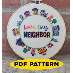 May include: A round embroidery hoop featuring a colorful embroidered design. The design includes various houses and the text "Love thy NEIGHBOR" in vibrant colors. A yellow banner at the bottom reads "PDF PATTERN".