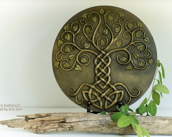 May include: A round, wooden wall plaque featuring a carved Celtic tree of life design. The tree is intricately detailed with leaves and branches, and the roots are intertwined in a knot pattern. The plaque is painted in shades of brown and gold.