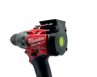 Puede incluir: Un taladro Milwaukee FUEL rojo y negro con un nivel adjunto en la parte superior. El nivel es verde y tiene una burbuja en el centro.