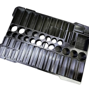 May include: Black plastic organizer tray with various compartments and circular holes. The tray is designed to hold and organize small items, with rectangular slots and round openings of different sizes.
