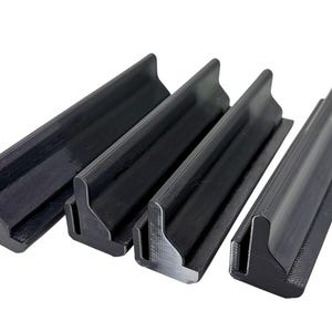 May include: Four black, angled, plastic shelf supports. Each support has a rectangular base and a raised, angled top. The supports are arranged in a row, with the tops facing the same direction.