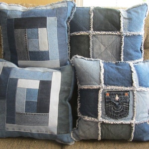 May include: Four denim patchwork cushion covers with frayed edges. The cushions are made from different shades of blue denim and feature a variety of stitching patterns. One cushion has a large pocket with a brand logo.