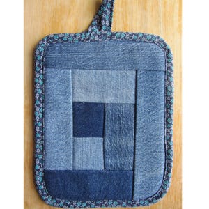 Puede incluir: Un salvamanteles cuadrado de mezclilla con un diseño de patchwork en varios tonos de azul. El centro presenta un patrón geométrico y los bordes están adornados con una tela estampada floral. Se adjunta un lazo para colgar.