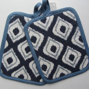 May include: A pair of blue and white patterned pot holders with a denim trim. The pot holders have a geometric design.