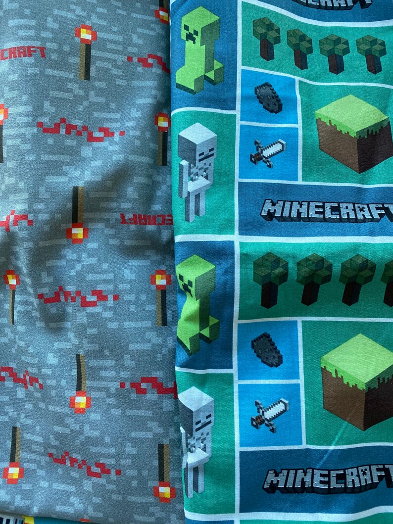 Puede incluir: Dos paneles de tela con tem&aacute;tica de Minecraft. Un panel es gris con antorchas rojas y la palabra "CRAFT". El otro panel es verde, azul y marr&oacute;n con im&aacute;genes de un creeper, un esqueleto, una espada, un bloque de tierra y la palabra "MINECRAFT".