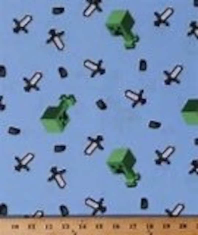 Puede incluir: Tela azul con un patr&oacute;n repetido de bloques de Minecraft verdes, espadas y diamantes negros.