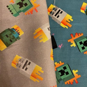 Puede incluir: Dos muestras de tela con un patr&oacute;n repetido de un personaje verde Minecraft Creeper con un dise&ntilde;o de llama amarilla. La tela de la izquierda es gris y la tela de la derecha es azul.