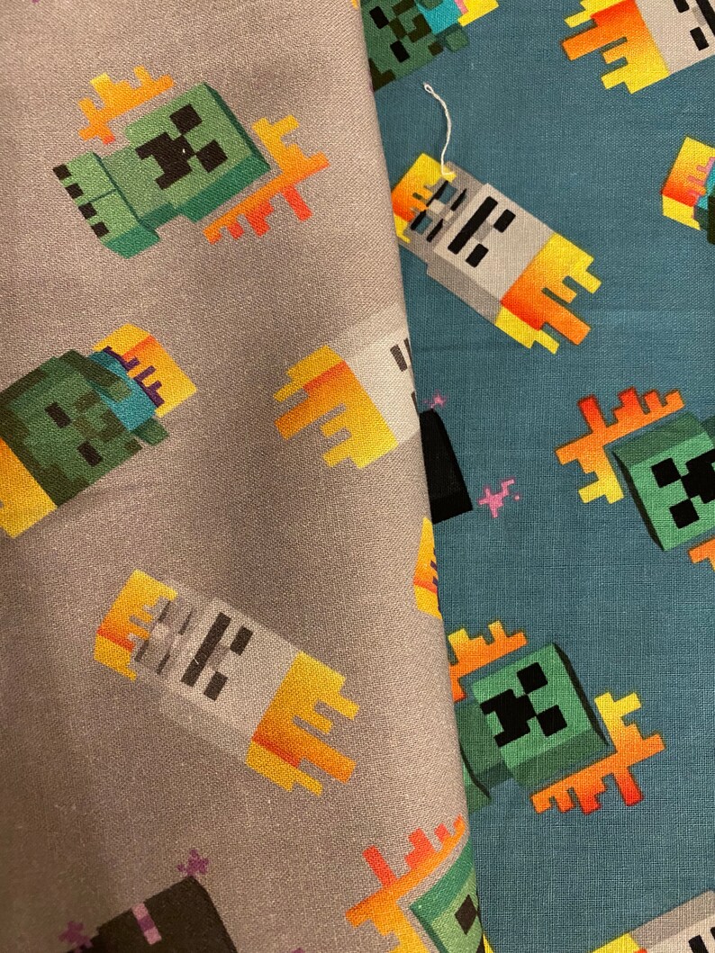 Puede incluir: Dos muestras de tela con un patr&oacute;n repetido de un personaje verde Minecraft Creeper con un dise&ntilde;o de llama amarilla. La tela de la izquierda es gris y la tela de la derecha es azul.