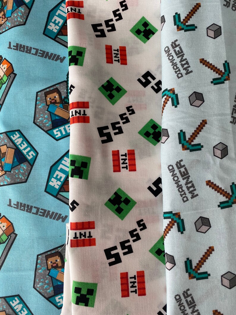 Puede incluir: Tres muestras de tela con dise&ntilde;os de Minecraft. La primera muestra es azul claro con un logotipo de Minecraft blanco y un patr&oacute;n repetido de picos y diamantes. La segunda muestra es blanca con un patr&oacute;n repetido de caras de Creeper verdes, 5 negros y bloques de TNT rojos. La tercera muestra es azul claro con un patr&oacute;n repetido de picos verdes y bloques grises.
