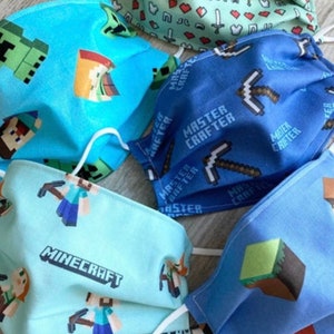 Puede incluir: Cuatro m&aacute;scaras faciales con tem&aacute;tica de Minecraft. Las m&aacute;scaras son azules, verdes, azul claro y verde claro. Las m&aacute;scaras tienen diferentes dise&ntilde;os, incluyendo un pico, un creeper y un personaje de Minecraft.