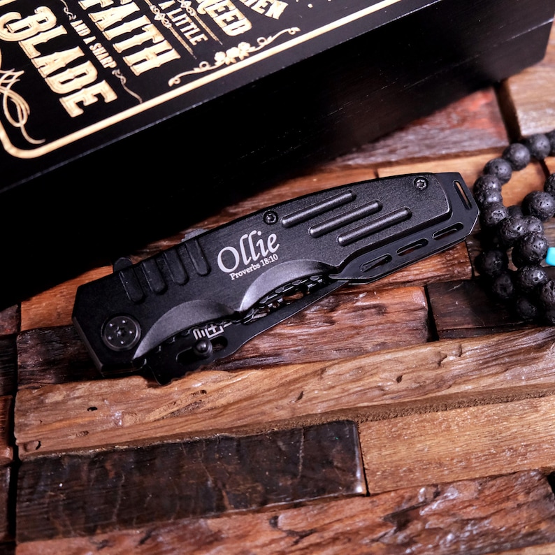 May include: Black pocket knife with a silver blade and a black handle. The knife is engraved with the name "Ollie" and the scripture "Proverbs 18:20".