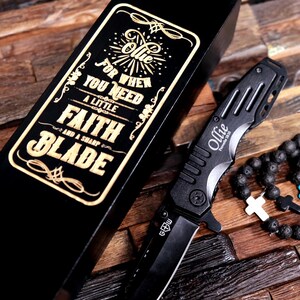 May include: A black wooden box with a gold inscription that reads "For when you need a little faith and a sharp blade." The box contains a black pocket knife with a silver blade and the name "Ollie" engraved on it.